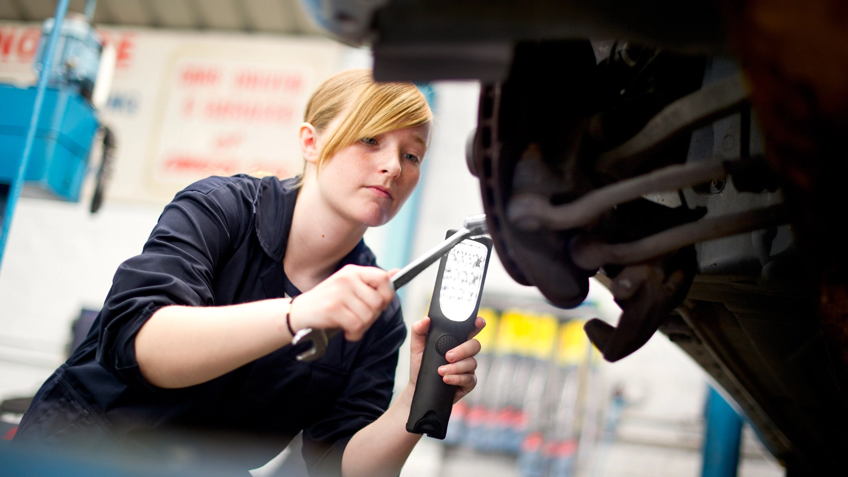 Auszubildende KFZ-Mechanikerin repariert ein Auto.